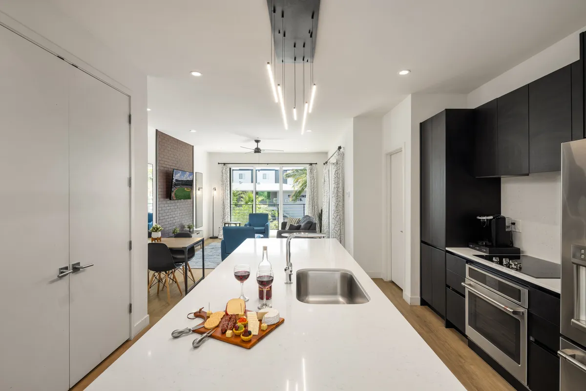 This image reveals the open-concept main living area, with the kitchen island, a charcuterie board set for entertaining, a welcoming dining area, and a comfortable living room framed by large windows. The seamless flow and natural light underline the inviting and social atmosphere described in the section.