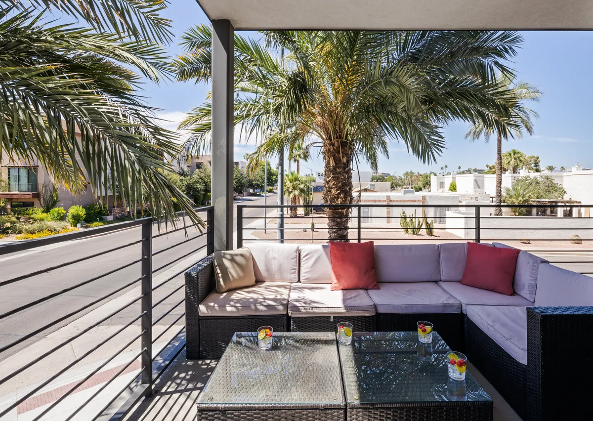 The image showcases a sun-drenched outdoor seating area framed by swaying palm trees, featuring a modern glass table with decorative cushions. The inviting space is perfect for relaxing, socializing, or enjoying a drink while taking in the Scottsdale sunset.