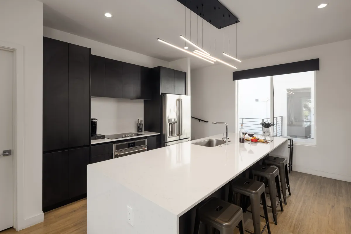 A bright, contemporary kitchen space with a generous island, modern light fixtures, and stainless steel appliances. The large window brings in natural light, making this a perfect spot for morning coffee or casual conversations.