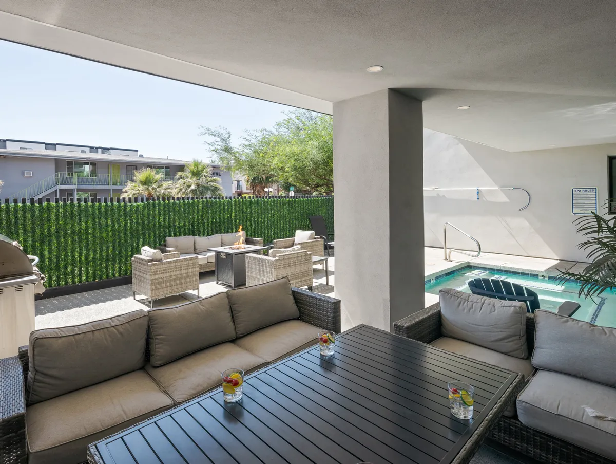 A resort-style outdoor space featuring a sparkling swimming pool surrounded by comfortable seating, lush greenery, and a table set with drinks. The area exudes a sense of relaxation and sociability, ideal for lounging, entertaining, or enjoying al fresco meals.