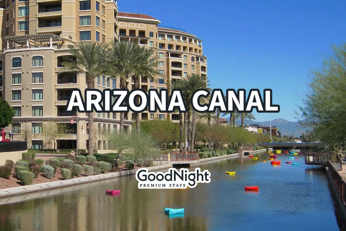 A colorful view of the Arizona Canal, with vibrant boats floating on the water, palm trees lining the path, and surrounding buildings creating a lively, accessible scene. People can be seen strolling and relaxing by the water.
