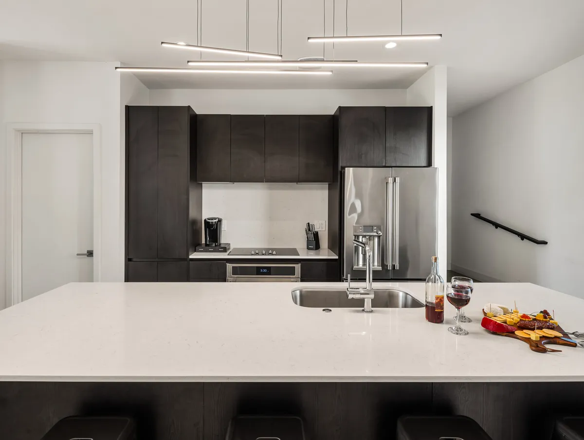 A modern kitchen scene featuring a spacious island countertop set with a bottle of wine, glasses, and a charcuterie board. Sleek, contemporary appliances are visible, and the ambiance is sophisticated yet relaxed—ideal for entertaining or group culinary activities.