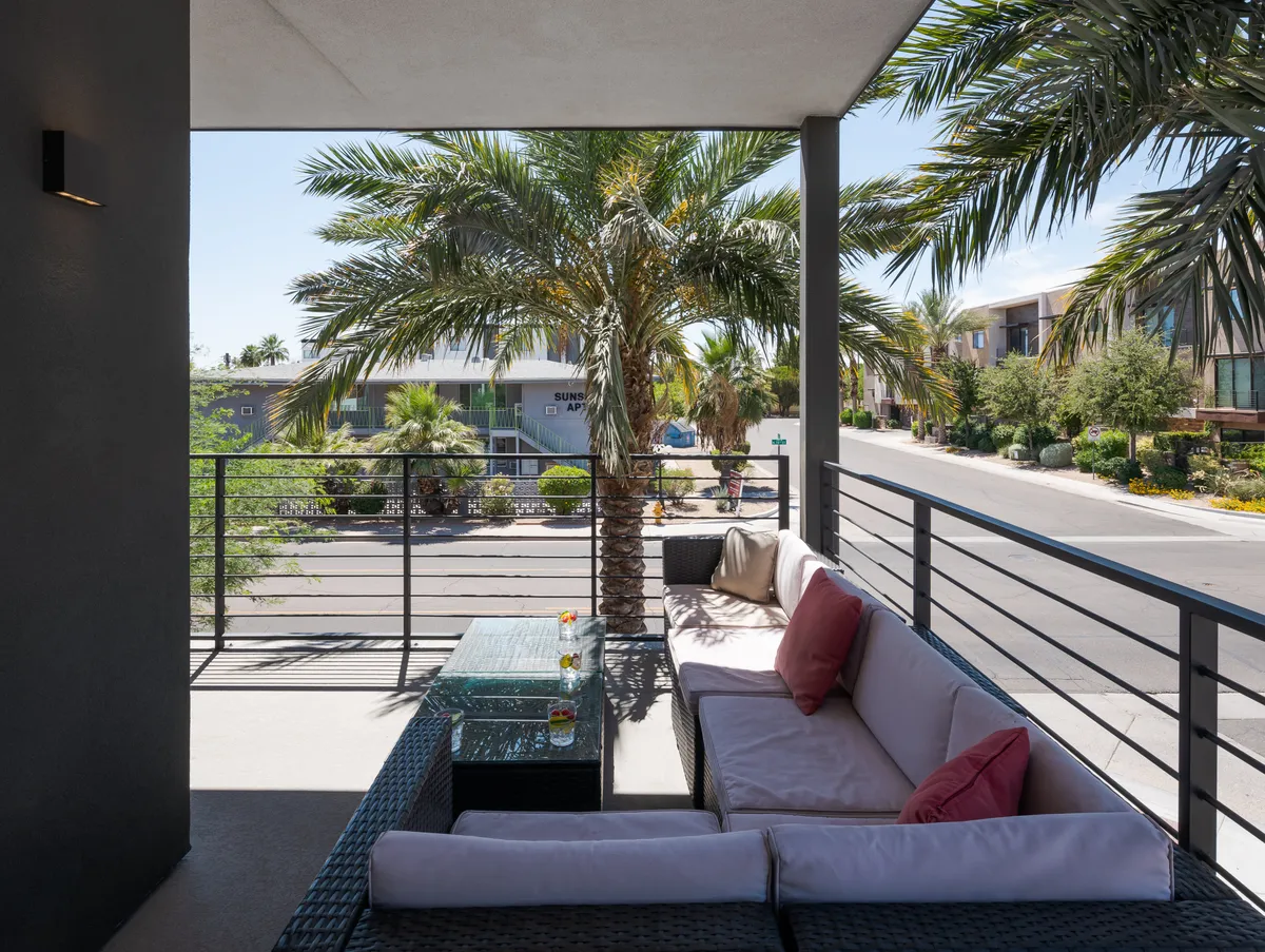 An inviting outdoor seating area framed by palm trees with a view of the street, where residents can relax with a drink, socialize, or enjoy the lively surroundings. The setting suggests a casual yet chic ambiance perfect for morning coffee or evening gatherings.